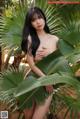 A naked asian woman posing in front of a palm tree.