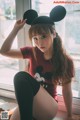 A woman wearing a mickey mouse ears hat sitting on a window sill.