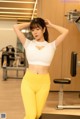 A woman in a white top and yellow leggings posing in a gym.