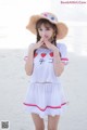 A woman in a white shirt and a straw hat on the beach.