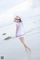 A woman in a white dress and hat standing on the beach.