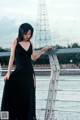 A woman in a black dress standing on a bridge.