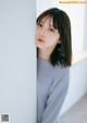 A woman leaning against a wall with her hand on her chin.