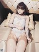 A woman in a white bodysuit sitting on a couch.