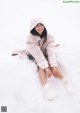 A woman sitting in the snow wearing a pink coat and white boots.