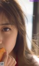 A woman eating a piece of food in front of a window.