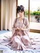 A woman in a pink kimono sitting on a bed.