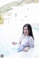 A woman in a white shirt leaning on the edge of a swimming pool.