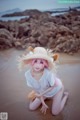 A woman with pink hair wearing a straw hat on the beach.