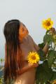 A naked woman standing in a field of sunflowers.