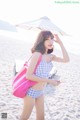 A woman in a bikini holding a pink bag on the beach.