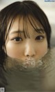 A woman in a bathtub with water on her face.